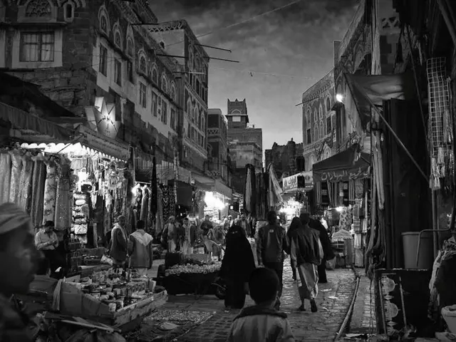 This is a black and white image. I can see groups of people walking. I can see few people standing....