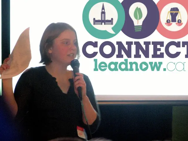 There is a lady holding mic and paper is talking. In the back there is a screen with something...