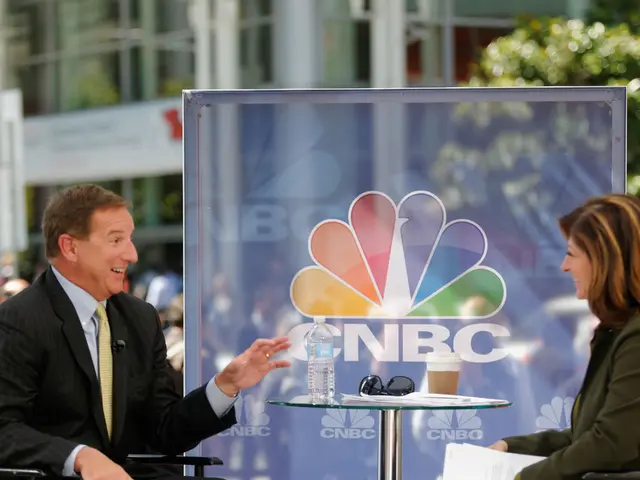 As we can see in the image there is building, tree, banner and few people sitting on chairs and...